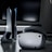 A sleek virtual reality headset sits on a reflective surface beside a gaming console and its controller. The background features a large dark monitor screen, creating a modern and futuristic setting. The lighting is subdued, highlighting the glossy surfaces of the electronic devices.